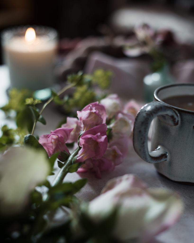 pink flowers & coffee cup with a lit candle in the background