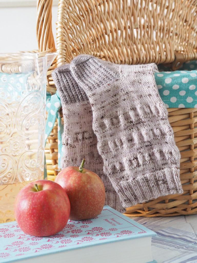 The Picnic Blanket Socks deigned by Helen Stewart/Curious Handmade, with a picnic basket and red apples