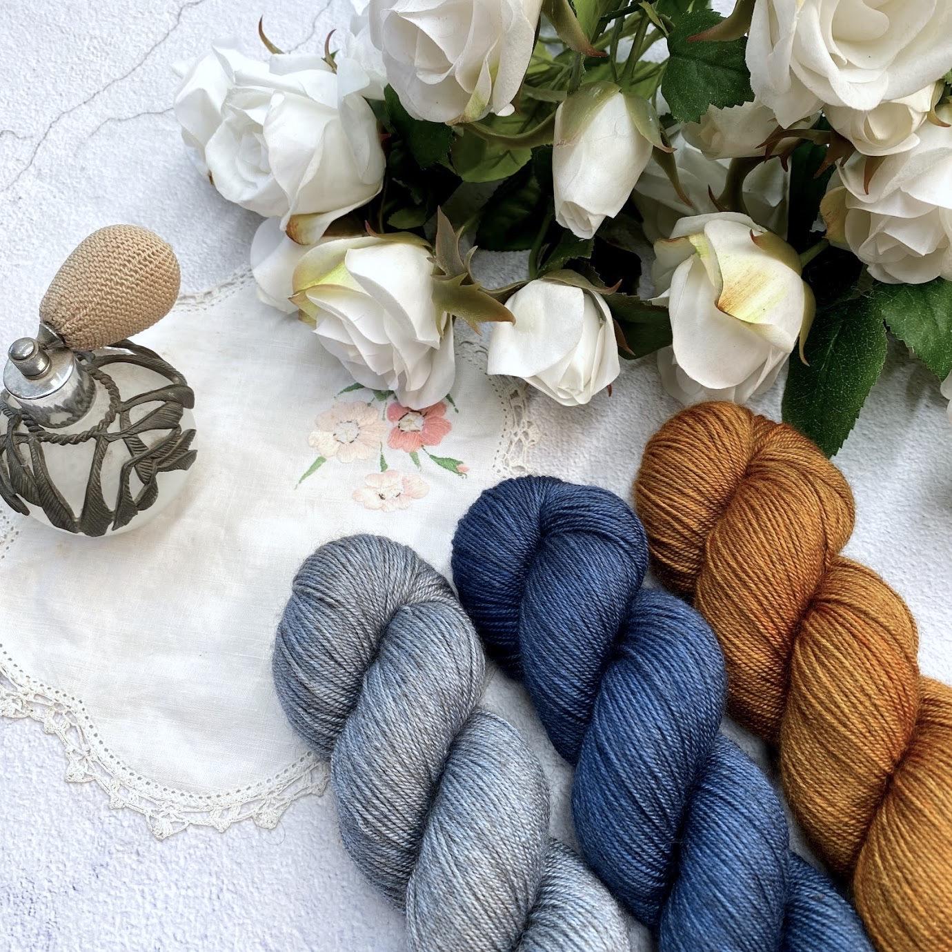3 Skiens of yarn in a grey, blue and yellow on a white background with some white roses