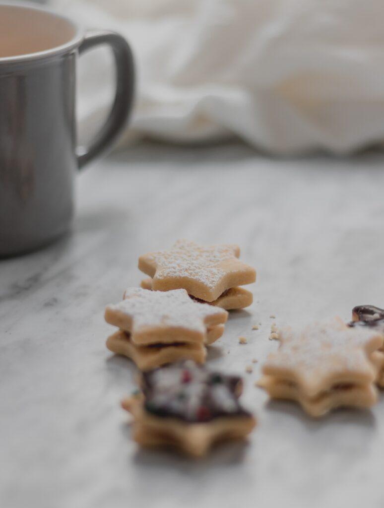 Star shaped sugar cookies on a table. In the background a grey ceramic mug is partially visual.