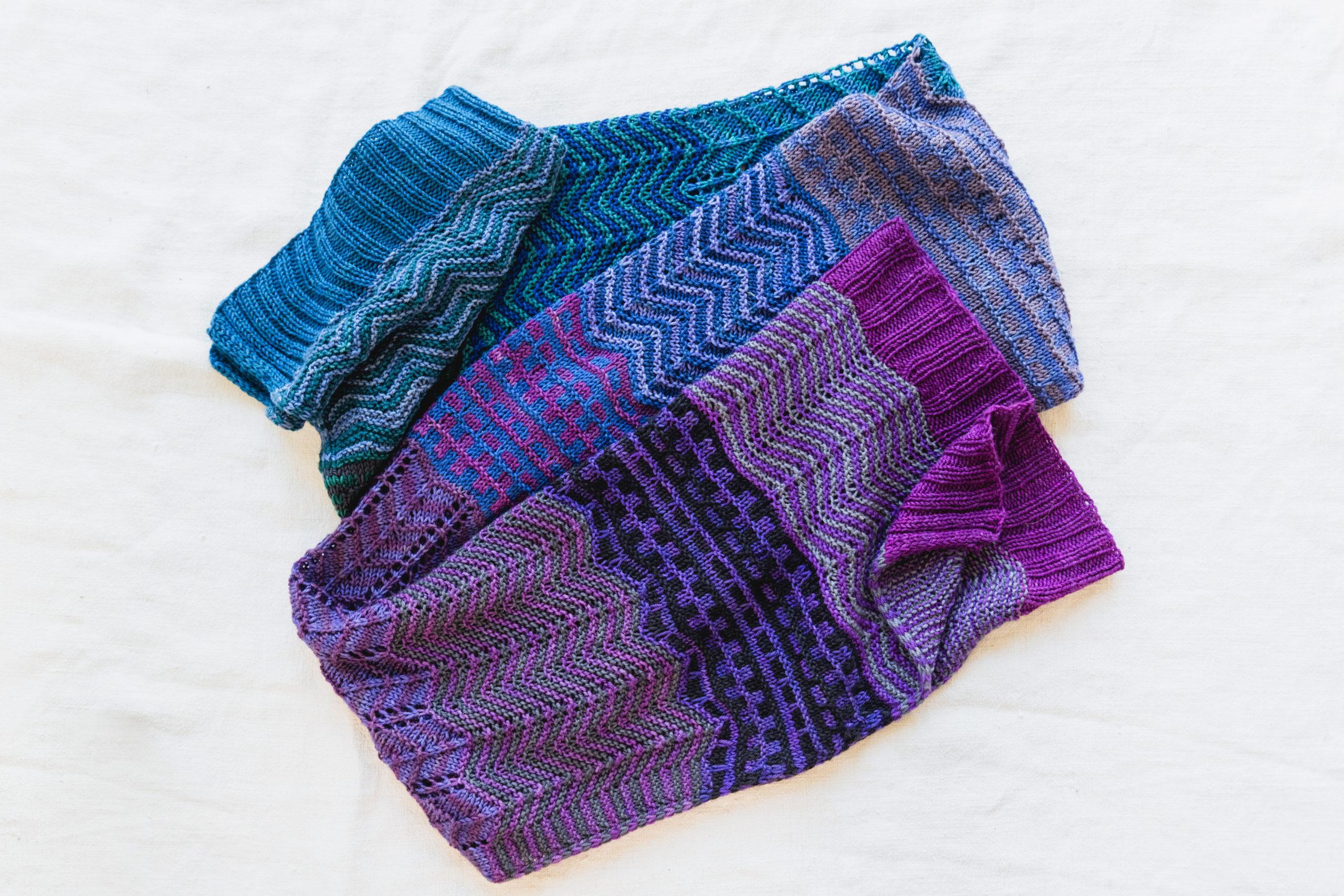 a long handknit wrap, The Skyline Wrap, scrunched up accordion style on a white background, knit in many shades of blue and purple