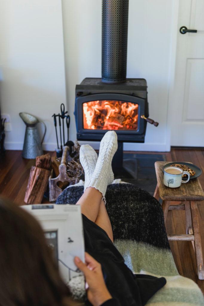 Person reading a knitting magazine warming in front of a lit firestove, wearing newly knitted Meet Cute socks