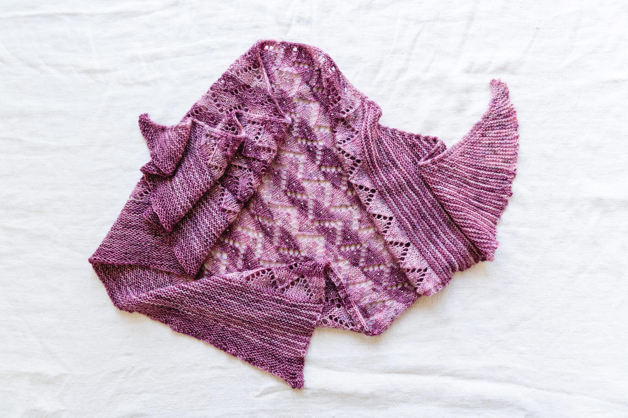 A handknit purple shawl with stripes of lighter pink and darker purple yarn, with a zigzag lace pattern and tiny sparkling beads knit into the fabric.