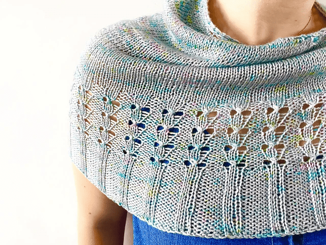 A close up of a shawl in soft pastels, wrapped around a person's shoulders