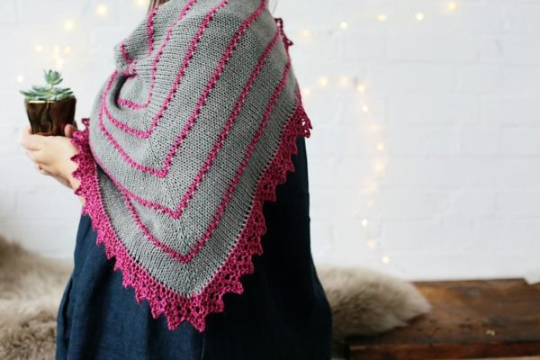 The Cabin Path shawl is grey with pink jagged trim and pink trianglular lines throughout the shawl.