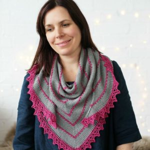 The Cabin Path shawl is grey with pink jagged trim and pink trianglular lines throughout the shawl.
