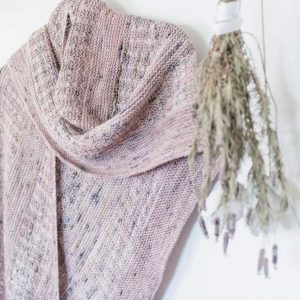 The Lavender Curling Mist Shawl is hanging up with a bunch of Lavender hanging unsidedown on the wall next to it.