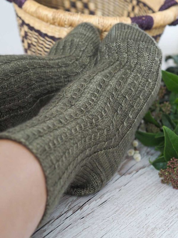 The Curling Mist Socks are a moss green knit, from the top-down with tiny cables and continue all over the leg and onto the top of the foot.