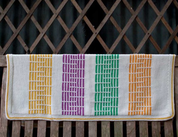 The Georgie Baby Blanket is a white with yellow, purple, green and orange pattern