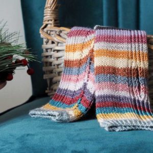 The Hearten Mitts are fingerless multi-coloured striped mitts sitting in a wicker basket