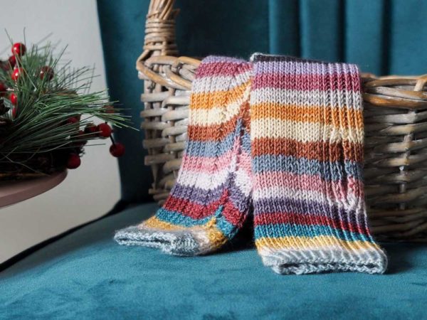 The Hearten Mitts are fingerless multi-coloured striped mitts sitting in a wicker basket