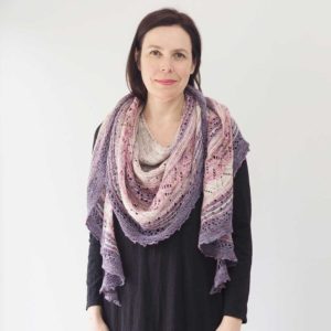 A multi-coloured artistic shawl, starting with creams and pinks and light to darker purples at the bottom of the shawl