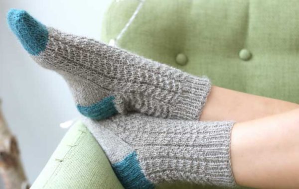 The Juniper Socks have a lovely textured rib stitch, the socks are knitting in light grey with a vibrant blue on the tow and heel.
