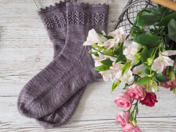 The Lavender Fields Socks are knit from the top down with a lavender-inspired lace panel around the top of the leg.