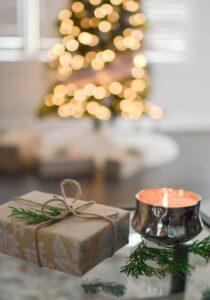 A candle and brown paper wrapped gift with blurred lights in background