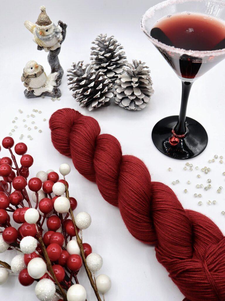 A dark red skein of yarn surreounded by christmas ornaments and a cocktail