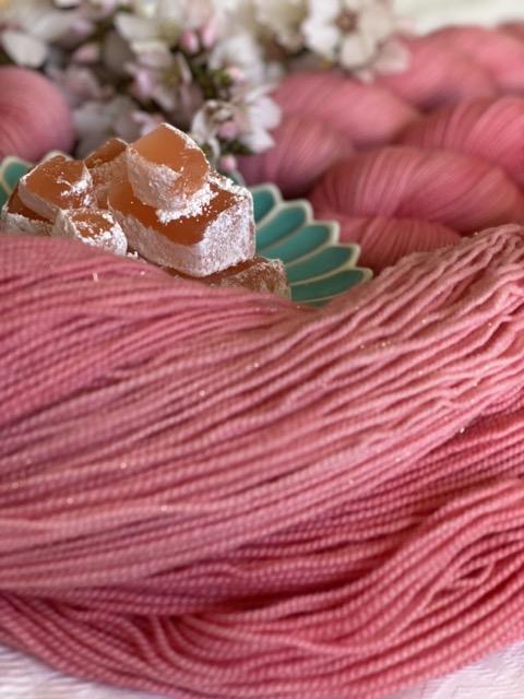 An unwound skein of pink yarn with a plate of Turkish delight and a blossoming branch