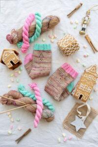Handknit socks and skeins of yarn in a flat lay with gingerbread houses and skeins of yarn