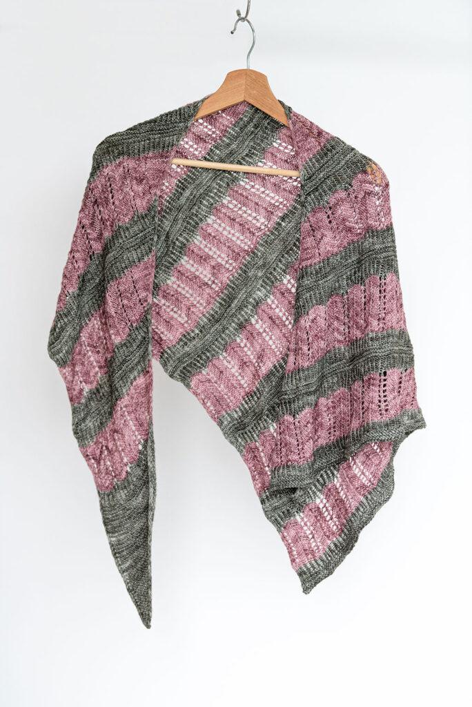 A handknit shawl with alternating bands of lace in grey and pink yarn