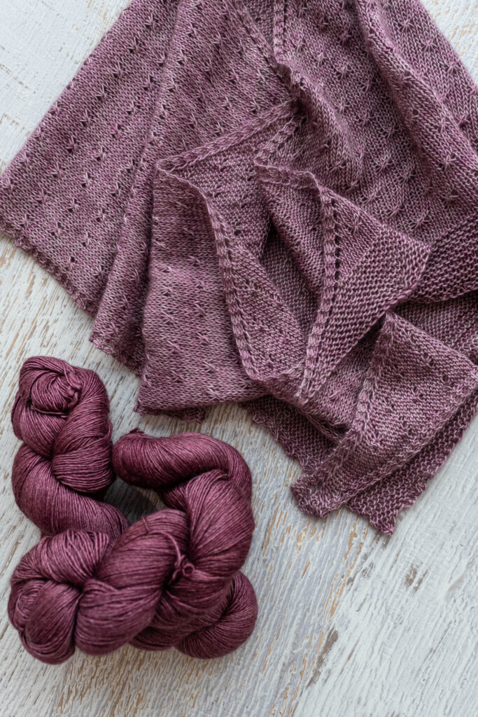 A pink knit shawl laying beside skeins of rich pink yarn