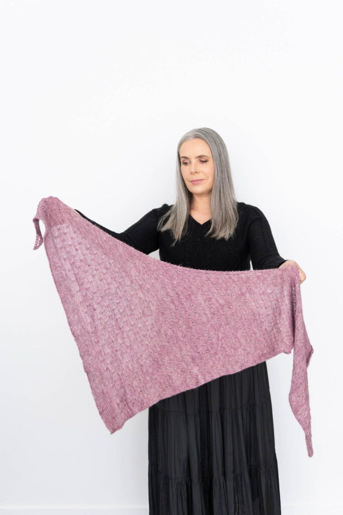 Helen holding out a pink  asymmetrical triangle shawl
