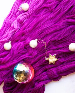 Five shades of magenta hand dyed yarn from Louie & Lola spread out with christmas baubles