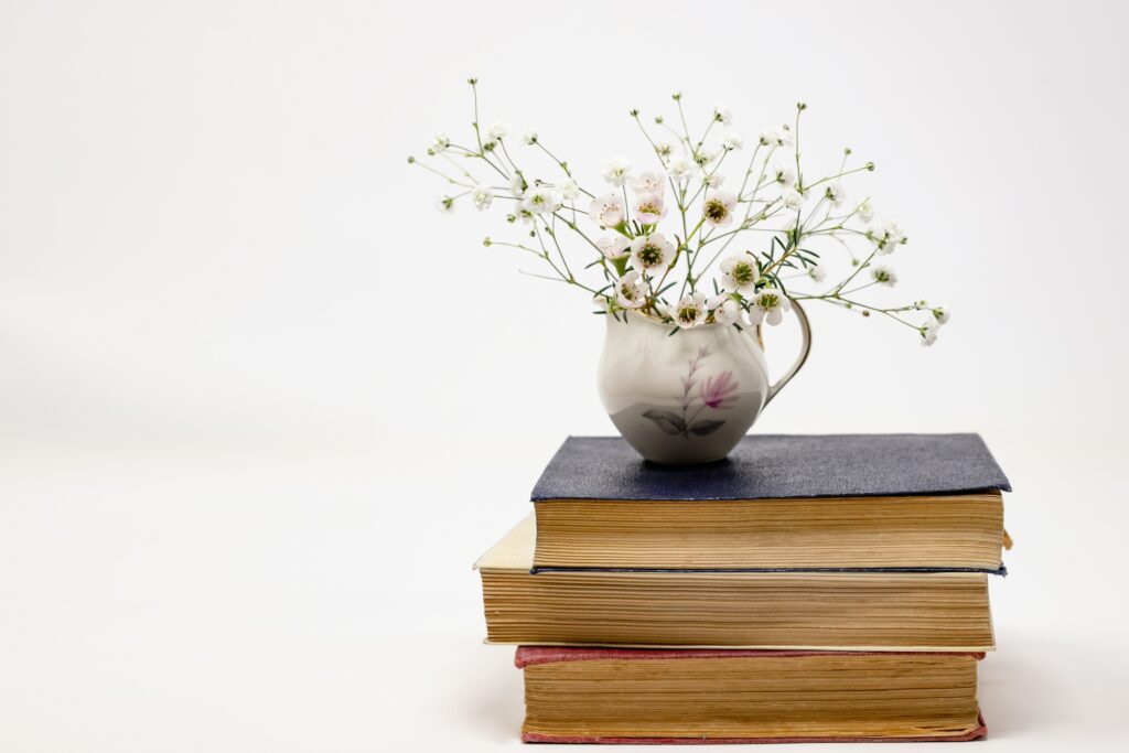 a small vase of white flowers on a stack of books, representing the theme of The Handmade Sock Society 6